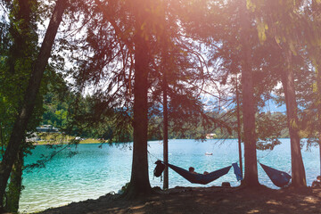 Silhouette of a man lie in the hammock near the lake. Calm, around the forest, silhouettes of trees, pine. Bled, Slovenia