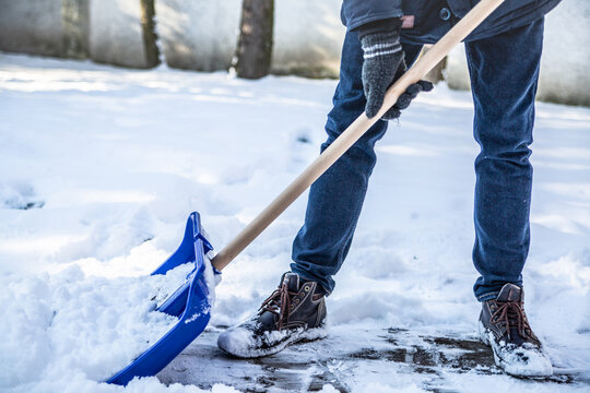 A Horizontal View Of Shoveling Snow From A Sidewalk With A Snow Shovel.