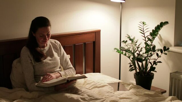 Woman reading book or Bible at night at home