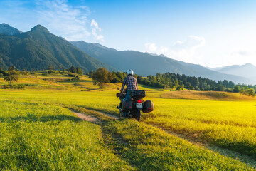 Man motorcyclist ride touring motorcycle. Alpine mountains on background. Biker lifestyle, world traveler. Summer sunny sunset day. Green hills. hermetic packaging bags. copy space. Slovenia