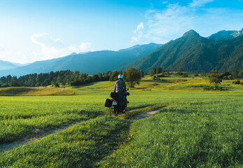 Man motorcyclist ride touring motorcycle. Alpine mountains on background. Biker lifestyle, world traveler. Summer sunny sunset day. Green hills. hermetic packaging bags. Slovenia