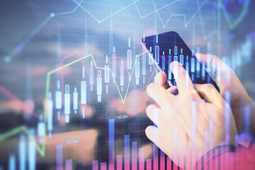 Double exposure of man's hands holding and using a digital device and forex graph drawing. Financial market concept.