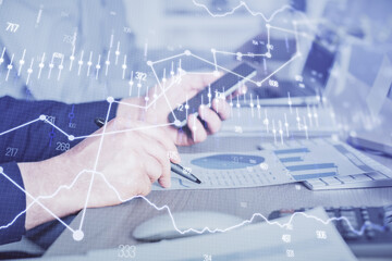 Double exposure of man's hands holding and using a digital device and forex graph drawing. Financial market concept.