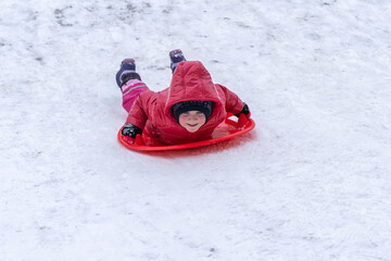 Fototapeta na wymiar A little girl rides a sled from a winter slide.