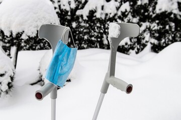 Schwieriges Terrain  für Gehbehinderte in Zeiten von Winter und  der Pandemie - Zwei Gehhilfen mit einer medizinischen Gesichtsmaske