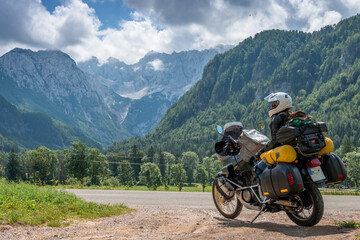 Fototapeta na wymiar Girl in full body protection, turtle armor, knee pads and helmet, tourer motorcycle for traveling with large luggage, on a background of green mountains, travel and freedom. Zgornje Jezersko Slovenia
