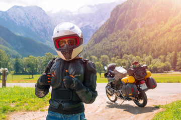 Woman in full body protection give like, turtle armor, knee pads and helmet, tourer motorcycle for traveling on a background. Green mountains, travel and freedom. Zgornje Jezersko Slovenia