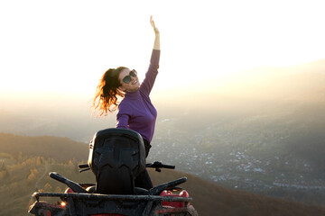 Young happy woman enjoying extreme ride on atv quad motorbike in autumn mountains at sunset.