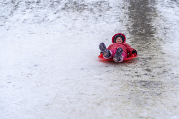Fototapeta na wymiar A little girl rides a sled from a winter slide.