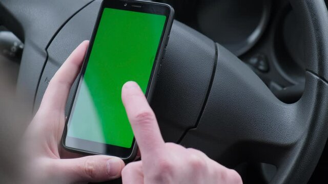 A man uses a smartphone with a green screen inside a car