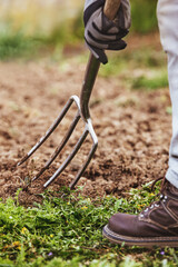 man is digging with a gardening fork in his garden