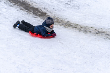 A little boy rides a sled from a winter slide.