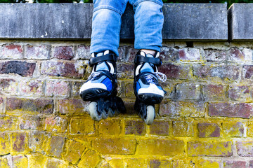 Child wearing jeans resting after roller blading sitting on the fence