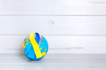 World globe with yellow and blue ribbon on wooden background. World Down Syndrome Day concept. Space for text.
