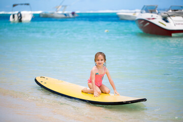 Little baby girl - young surfer with bodyboard has a fun on small ocean waves. Active family...