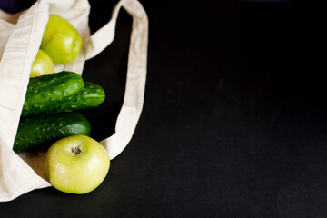 Cotton bag with green fresh bright vegetables and fruit on a black background.