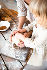Cute little girl and her beautiful mom make dough in a bowl stay at home.