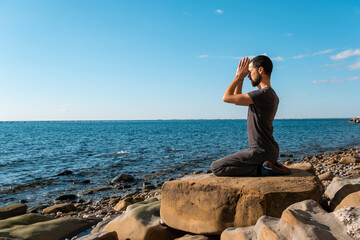 Attractive young man practicing yoga meditation and breathwork outdoors by the sea