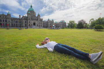 Fototapeta premium A young woman relaxes on the grass in front of the Legislative Assembly of British Columbia on a sunny summer day in Victoria, Canada.