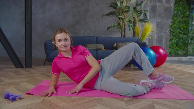 Motivated active lifestyle sporty fit attractive woman lying on yoga mat, performing clamshell leg workout, toning inner and outer thighs, hamstring muscles while exercising in domestic room.