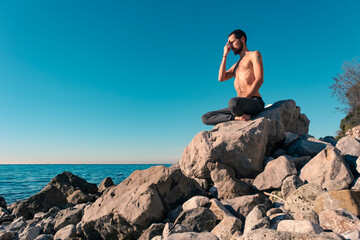 Attractive young man practicing yoga meditation and breathwork outdoors by the sea