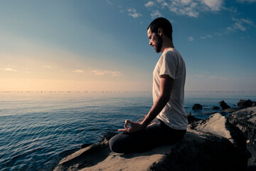 Fototapeta na wymiar Attractive young man practicing yoga meditation and breathwork outdoors by the sea