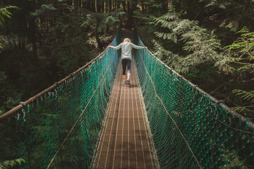 A young woman crosses a rainforest suspension bridge on the Juan de Fuca trail on the way to Mystic Beach on Vancouver Island, British Columbia in the pacific northwest Canada.