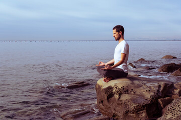 Attractive young man practicing yoga meditation and breathwork outdoors by the sea