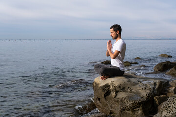 Attractive young man practicing yoga meditation and breathwork outdoors by the sea
