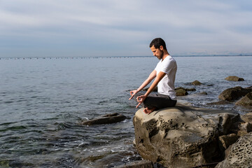 Attractive young man practicing yoga meditation and breathwork outdoors by the sea
