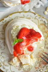 Mini meringue with strawberries poured with syrup on a rustic plate