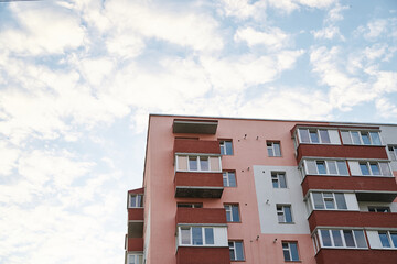 View from underneath on colorful pink apartment building in front of blue sky with clouds. City dwelling. Urban architecture concept.