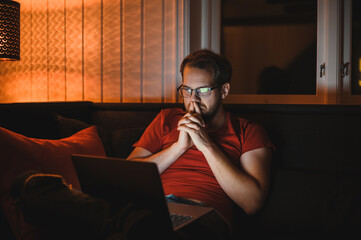 Portrait of attractive nerdy man is working late night on the computer in living room in home office
