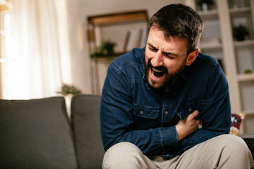 Fototapeta premium Sick man at home. Young man sitting on sofa having fever