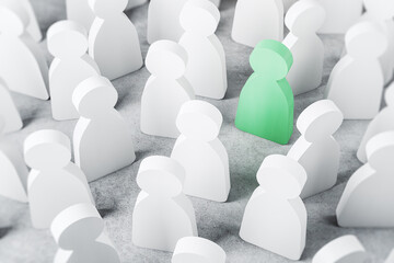 Green wooden figure as unique and talented person in business team stands in a crowd of white wooden figures as herd-minded people on concrete table. 