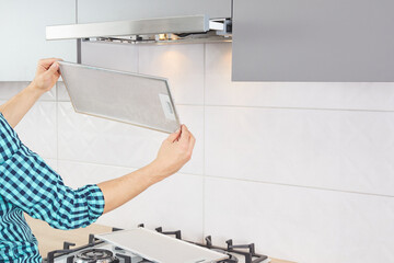 Mans hands removing a filter from cooker hood for cleaning or service. Replacing filter in kitchen...