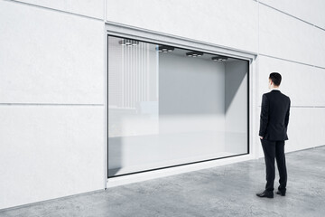 Businessman in black suit looking at empty street shop window in light building outside. Mockup