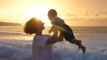 Young mother spinning her baby at the beautiful sun by the ocean © Sia