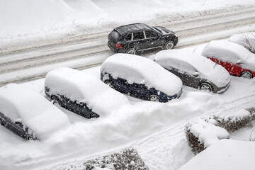 Snow covered cars in the parking lot on the city street. A car driving on a snow covered road. Winter season