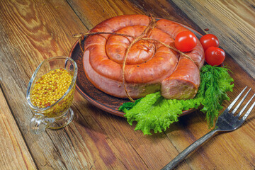 Smoked sausage, twisted in a spiral in a plate of herbs on an old rustic wooden table.Homemade food.Selective focus.