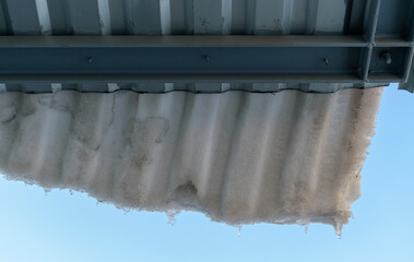 Snow falling from the metal roof. Concept of the danger of falling snow and icicles from the roofs of houses and buildings.