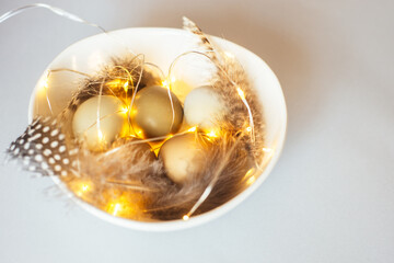 Stylish Easter festive eggs in natural color on a light background with garlands, feathers in bowl white.