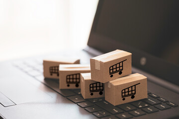 Fototapeta premium Trolley or shopping cart logo on small cartons boxes lay on keyboard computer laptop for online shopping and service delivery to customer concept.