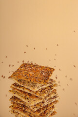 A stack of healthy flaxseed cookies on top of which the seeds are poured on a neutral beige background