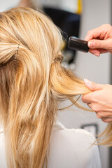 Fototapeta premium Rear View of a hairdresser combs blonde hair of the young woman in a beauty salon