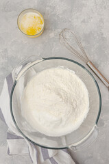 Whipped egg whites with flour in a bowl on a gray concrete background. Cooking a vanilla cake with blueberries. Recipe step by step. Top view.