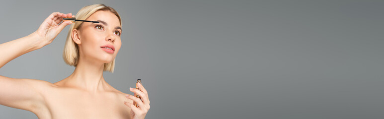 Obraz premium Low angle view of young woman holding mascara isolated on grey, banner