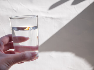 水が入った透明グラスを持つ手。水分補給、水を飲む。