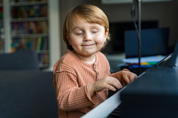 Close up portrait of adorable little toddler boy. Smiling child playing piano at home. Kid learning  play music. Early development.