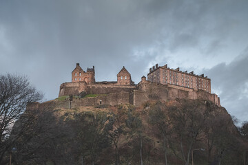 Fototapeta na wymiar The historic Edinburgh Castle perched atop Castlehill against a moody backdrop on a dark evening in Scotland.